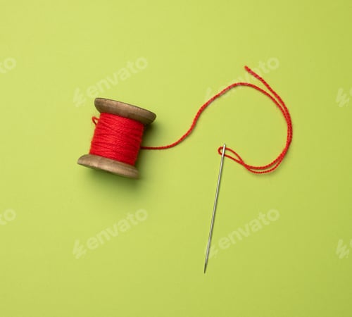 Preview: Wooden spool with red wool thread on a green background