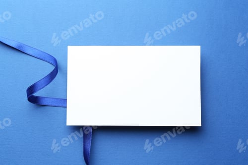 Preview: Beautiful ribbon and blank card on blue background, flat lay
