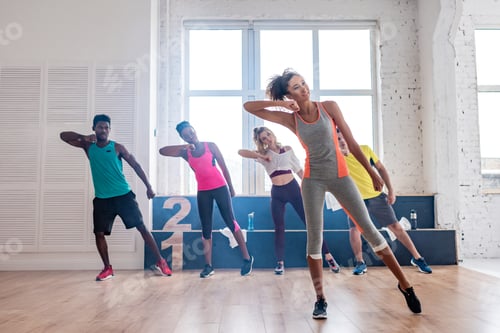 Preview: Smiling african american trainer performing zumba with multicultural dancers in dance studio