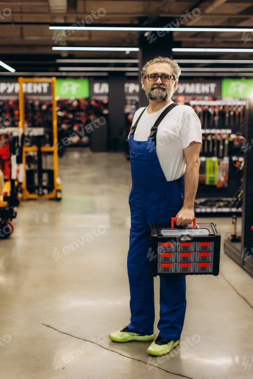 Preview: Smiling craftsman man carrying toolbox in hardware store