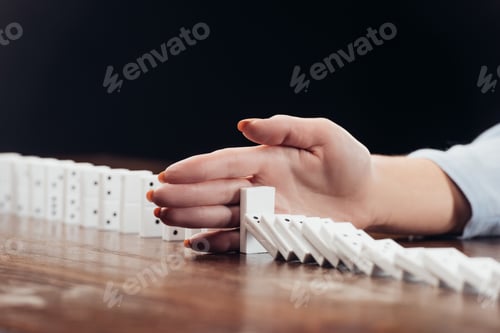 Preview: cropped view of woman preventing dominoes from falling on desk isolated on black