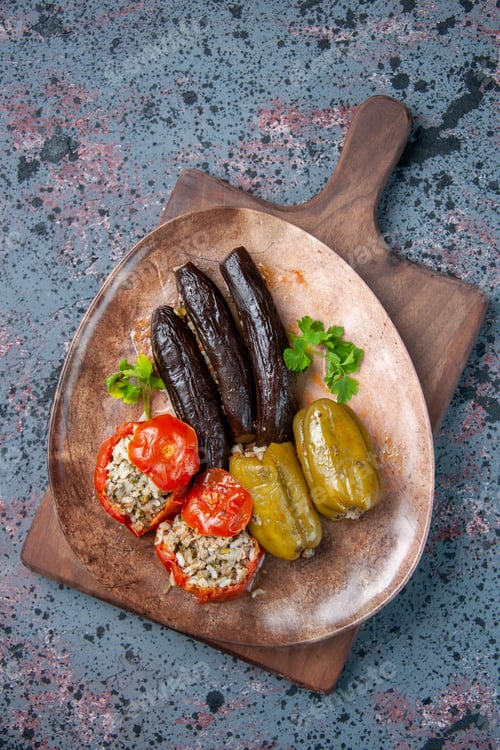Preview: top view eggplant dolma with cooked tomatoes and bell-peppers filled with ground meat on blue
