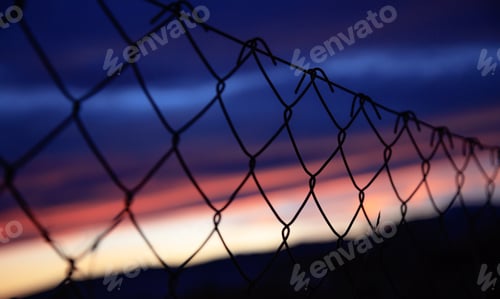 Preview: Wire mesh fence on silhouettes of poles on sky blur background at sunset
