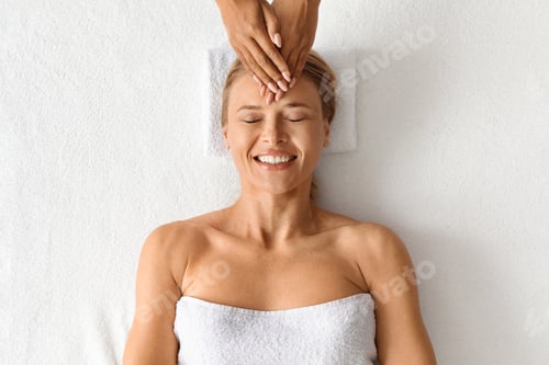 Preview: Beautiful middle aged woman relaxing during acupressure head massage at spa salon