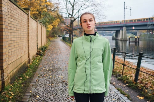 Preview: Attractive sporty girl listening music in earphones after run in autumn park