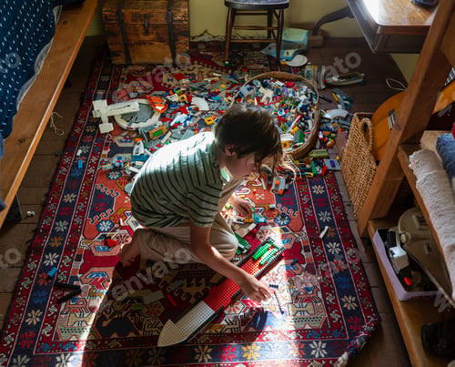 Preview: Boy sitting among toys on his bedroom floor in a patch of sunlight