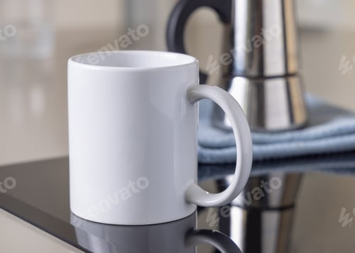 Preview: White coffee mug on induction stove against moka pot on blue dish cloth closeup, mockup