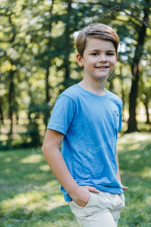 Preview: portrait of adorable child standing with hands in pockets and smiling at camera in park