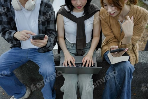 Preview: Group of young adults are sitting together outside, using a laptop, smartphone