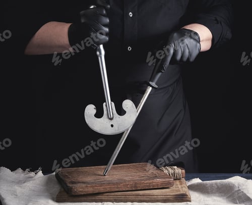 Preview: Male cook in black uniform and black latex gloves holds a large sharp vintage knife