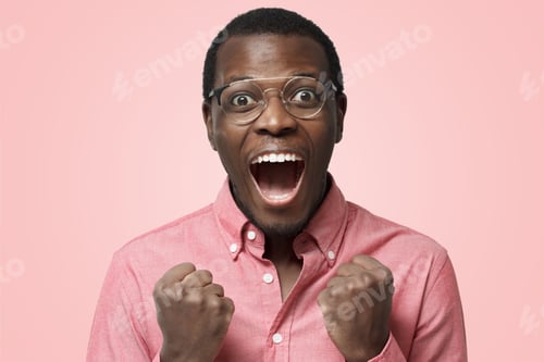 Preview: Attractive african man shouting while his team wins raising both fist in victory gesture