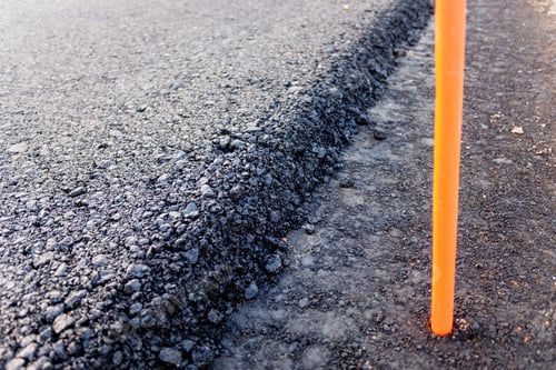 Preview: Detail of the edge of a freshly paved road with marking sticks.