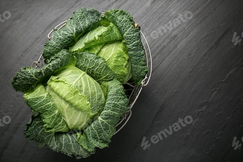 Preview: Fresh Savoy cabbages in metal basket on black table, top view. Space for text