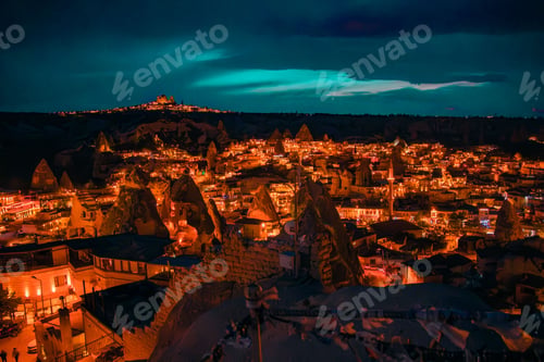 Preview: Nighttime vertical image of a quaint town nestled in a valley, illuminated by lights