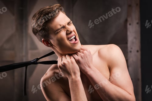 Preview: Got you! Frustrated young man choking by his necktie while standing against metal background