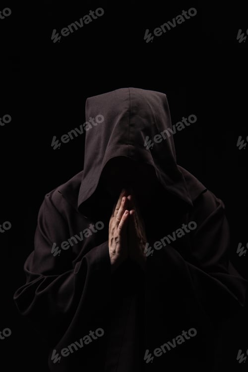 Preview: monk in hooded robe with praying hands and obscured face isolated on black