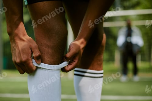 Preview: Man Adjusting Socks on Soccer Field before Training Session