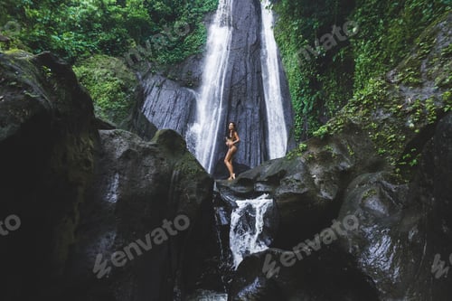 Preview: Woman enjoying near hidden in jungle cascade waterfall in Bali. Slim body and black swimsuit