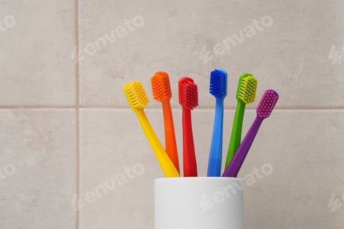 Cepillos de dientes multicolores. Seis cepillos de dientes brillantes en un vaso blanco en el baño. Arcoíris.