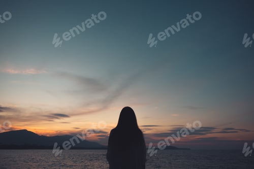 Preview: Silhouettes of a woman looking at view on the beach with sea and sunset background