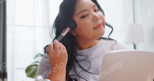 Preview: A chubby Asian woman practicing beauty makeup while relaxing at home.