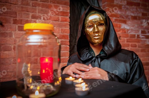 Preview: Closeup shot of a girl in golden mask and black hooded costume during a ceremony with candles