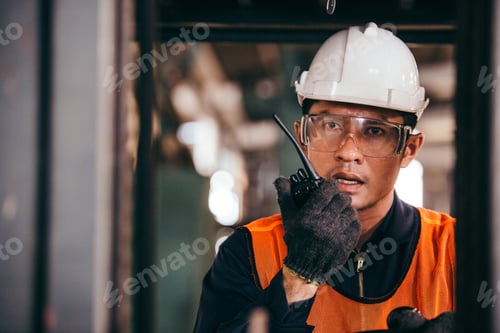 Preview: Asian male warehouse worker talking on radio phone driving forklift