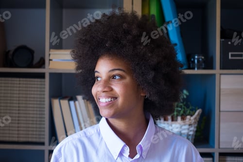 Preview: Attractive dark skinned young woman with curly Afro hairstyle looking out through window.