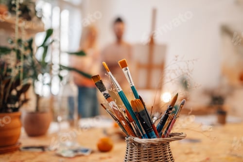 Preview: Paintbrushes in creative atelier with couple painting in background.