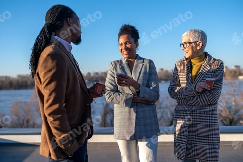 Preview: Mid-adult multiethnic business executives enjoy a sunny coffee break on top an office building