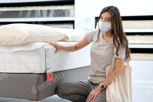 Preview: Woman wearing protective mask selecting bed mattress