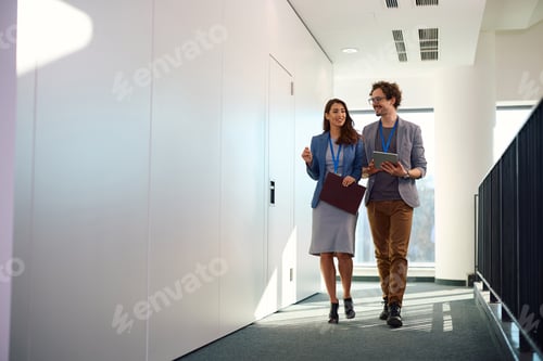 Preview: Happy business colleagues talking while walking through hallway of an office building.