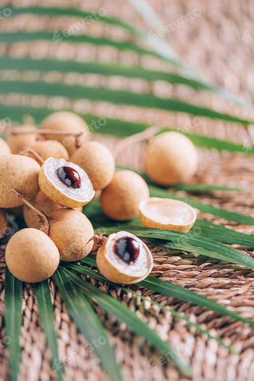 Preview: Longan fruits over palm leaves on rattan background. Copy space. Dimocarpus longan. Bunch of exotic
