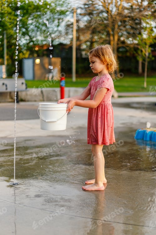 Preview: Child playing with water and bucket at splash pad playground in park. Girl having fun in summer