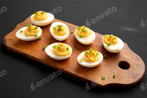 Preview: Homemade Deviled Eggs with Chives on a rustic wooden board on a black background, side view.