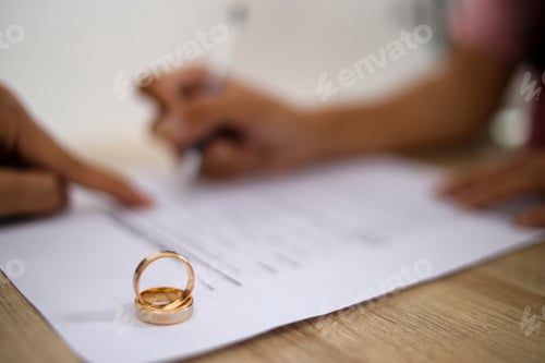 Preview: Wedding Rings Against Woman Hand Filing Divorce Papers or Premarital Agreement Prepared by Lawyer