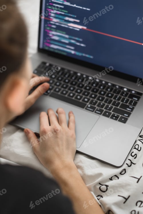 Preview: Young female programmer writes program code on a computer laptop in the bed at home. remote work