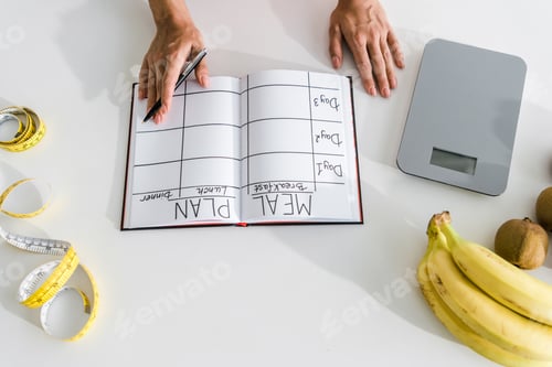 Preview: cropped view of woman holding pen near notebook and fruits