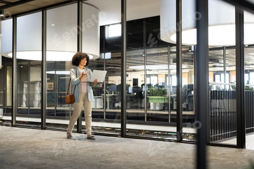 Preview: Walking in modern office, woman holding laptop and wearing business attire, copy space