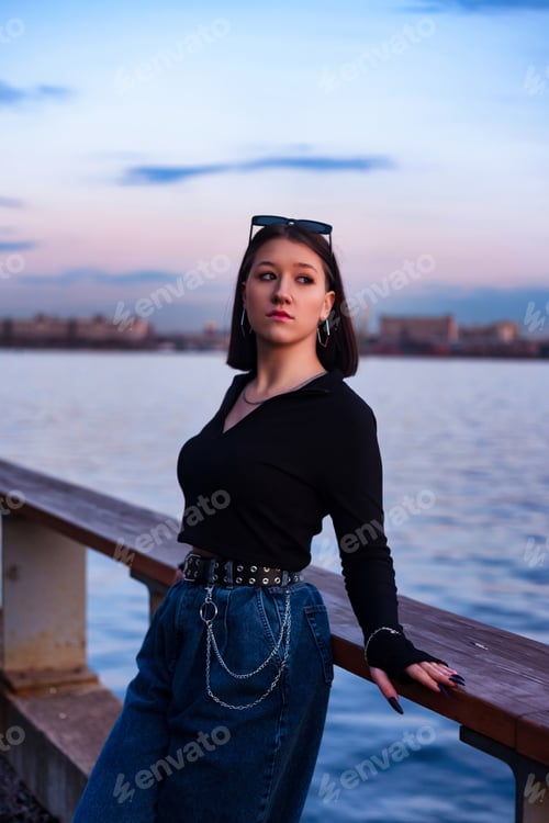 Preview: Teenage Girl Stands by the Water in an Industrial Area at Dusk, Looking Thoughtful