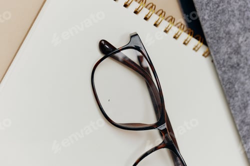 Preview: Closeup cropped shot of brown stylish classic unisex eyewear leans on notebooks on over pastel beige