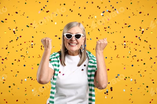 Preview: Excited senior woman on yellow background with flying confetti