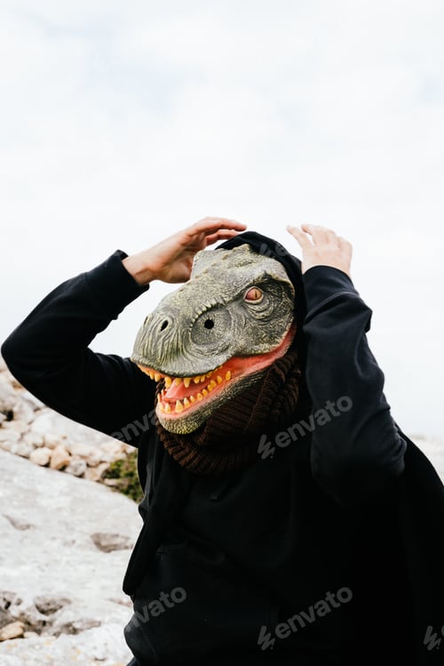 Preview: Caucasian man wearing a dinosaur mask and a cape surprised and holding his hands to his head
