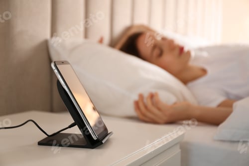 Preview: Smartphone charging on wireless pad and woman sleeping in bed