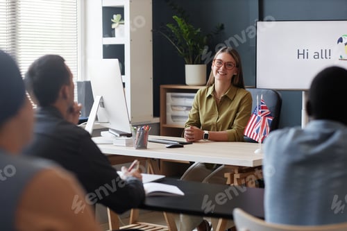 Preview: Smiling Woman Talking to Student Teaching English at Desk in Language Course Class