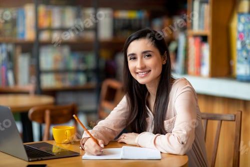 Preview: Enthusiastic student latin lady looking for job online, using laptop and taking notes, sitting at