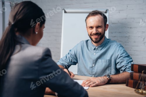 Preview: selective focus of bearded man signing insurance agreement near brunette lawyer