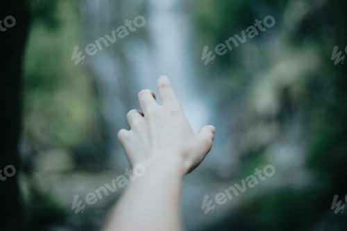 Preview: Moody image of an selective in focus hand in front of a waterfall during a sunny day