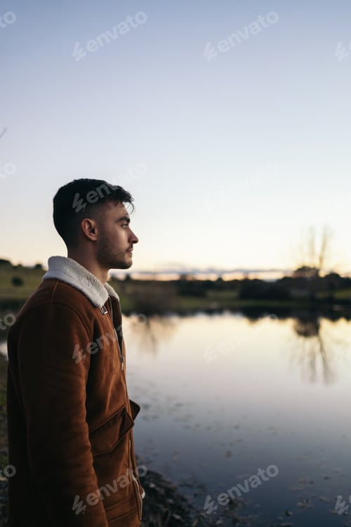 Preview: Young man watching the sunset at a lake in the countryside