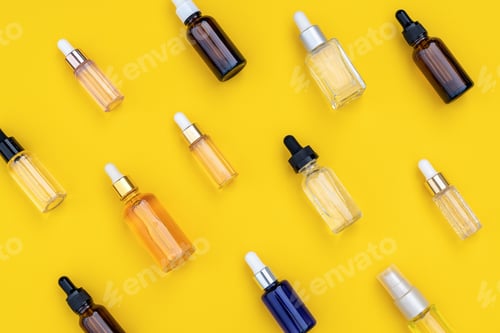 Preview: Abstract pattern of serums in glass bottles with dropper on bright yellow background.